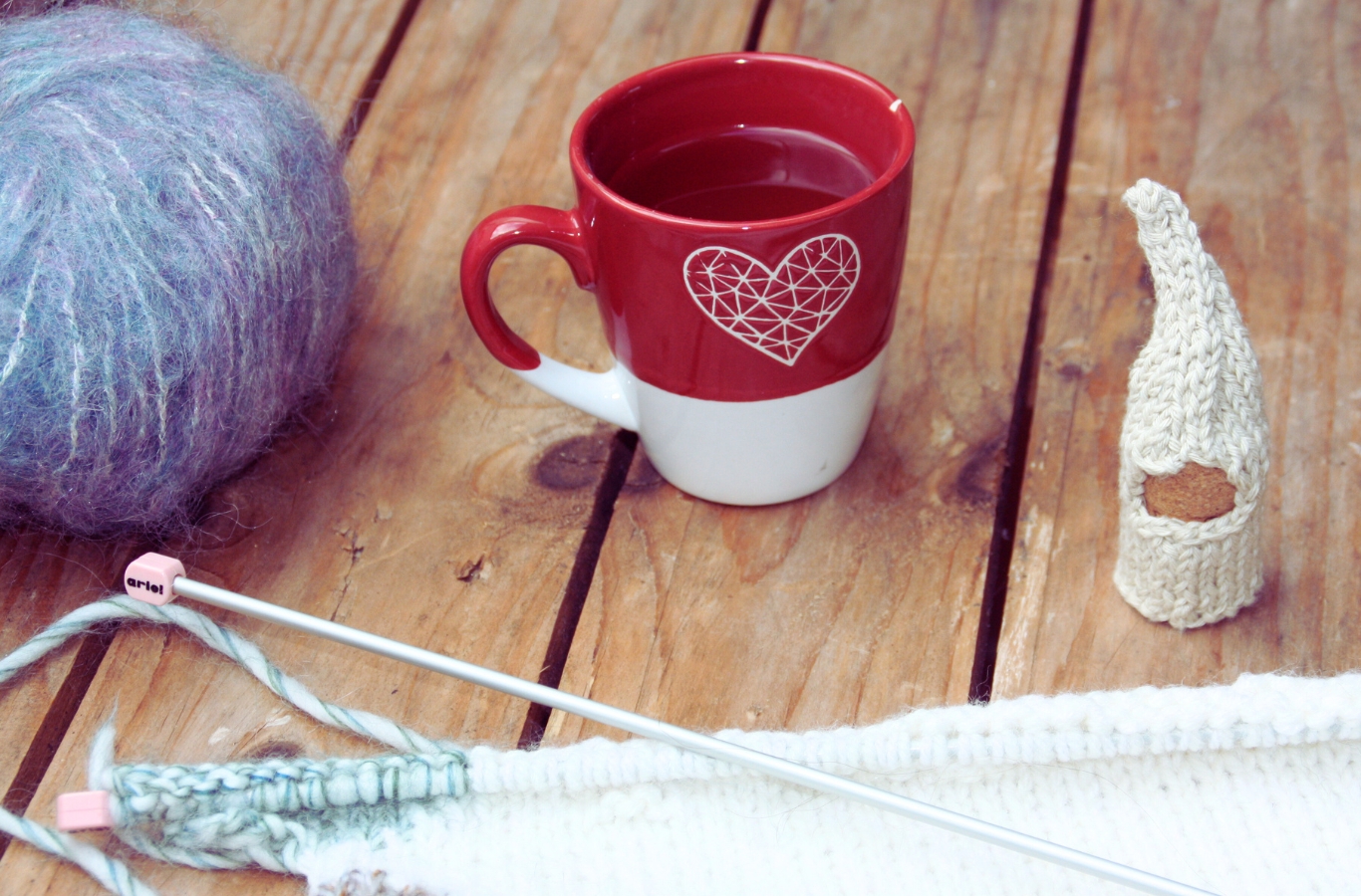 Table avec tasse de thé, pelote de laine, ouvrage en cours et lutin blanc tricoté par Karen Lambert